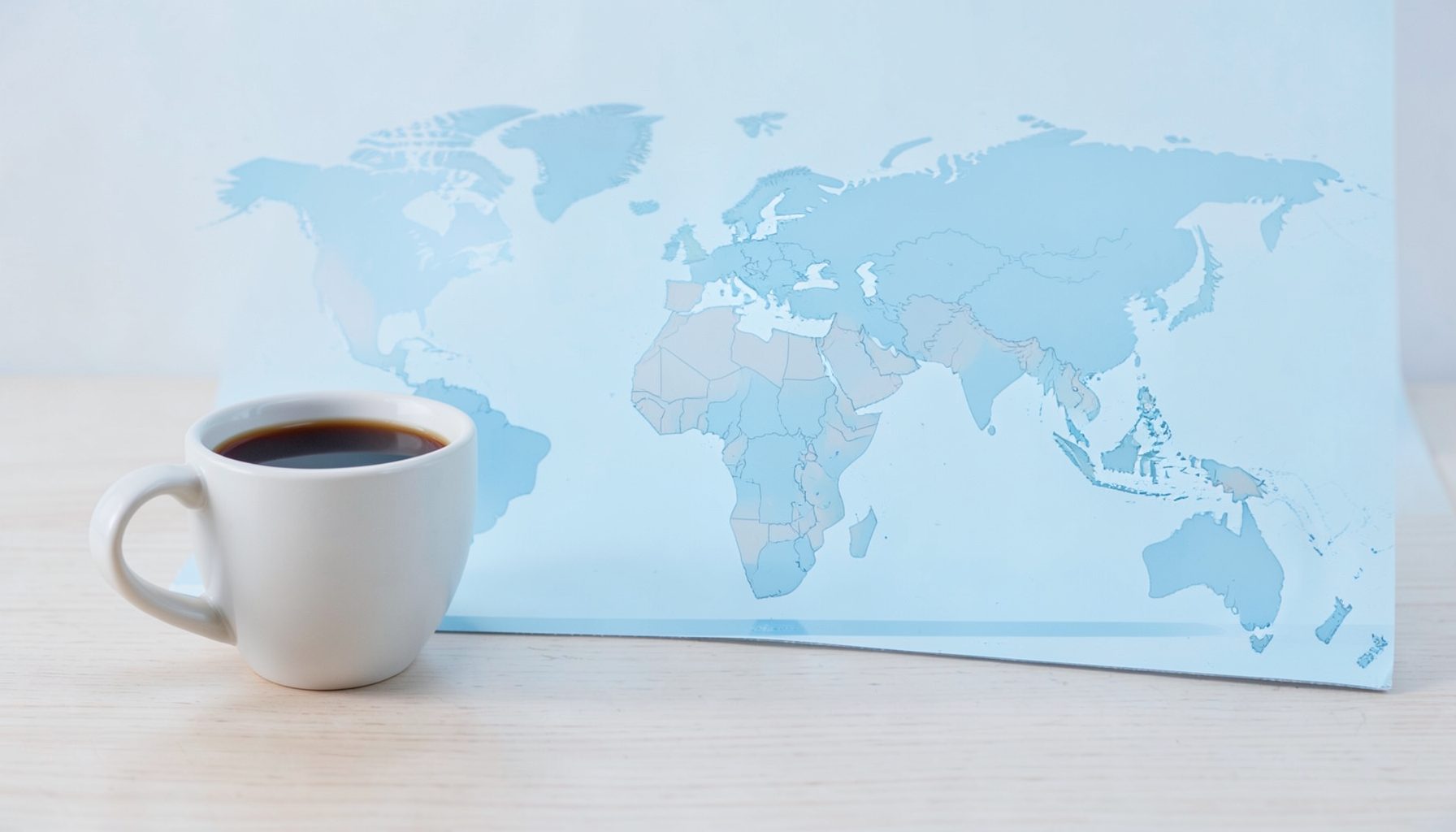 Mapa-múndi em tons suaves de azul e bege sobre uma mesa, com uma caneca de café ao lado, sugerindo alcance internacional e comunhão fraternal.